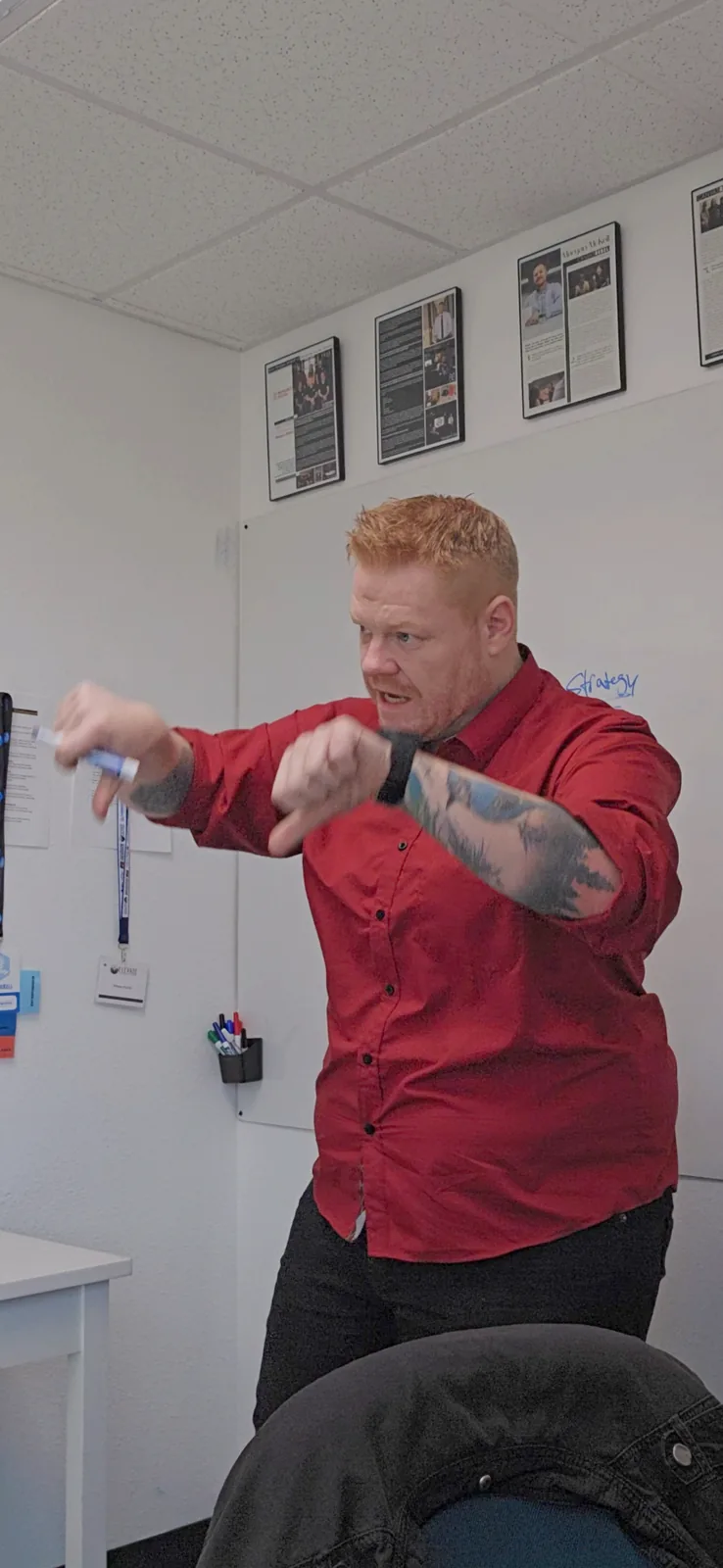 Morgan McKell at the whiteboard mid strategy session, framed press features on the wall behind him
